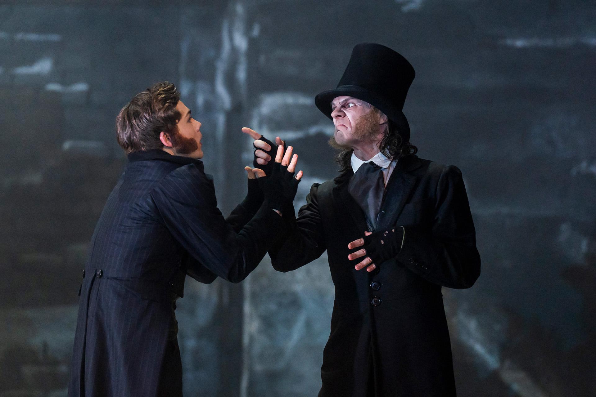Scrooge frowns and points menacingly at a scared Bob Cratchit
