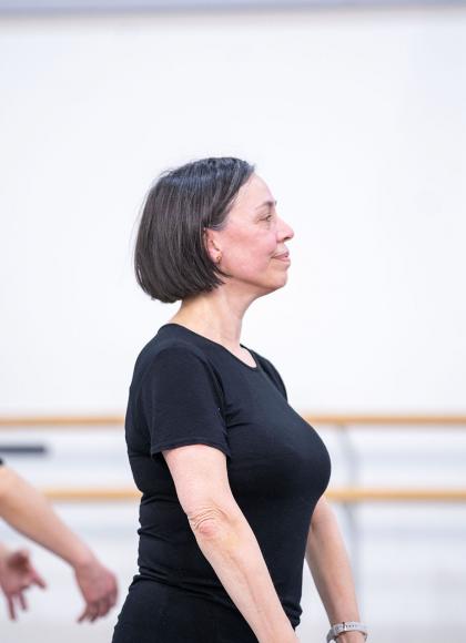 Woman in profile, wearing black T-shirt with darker bobbed hair, striking classic ballet pose in class
